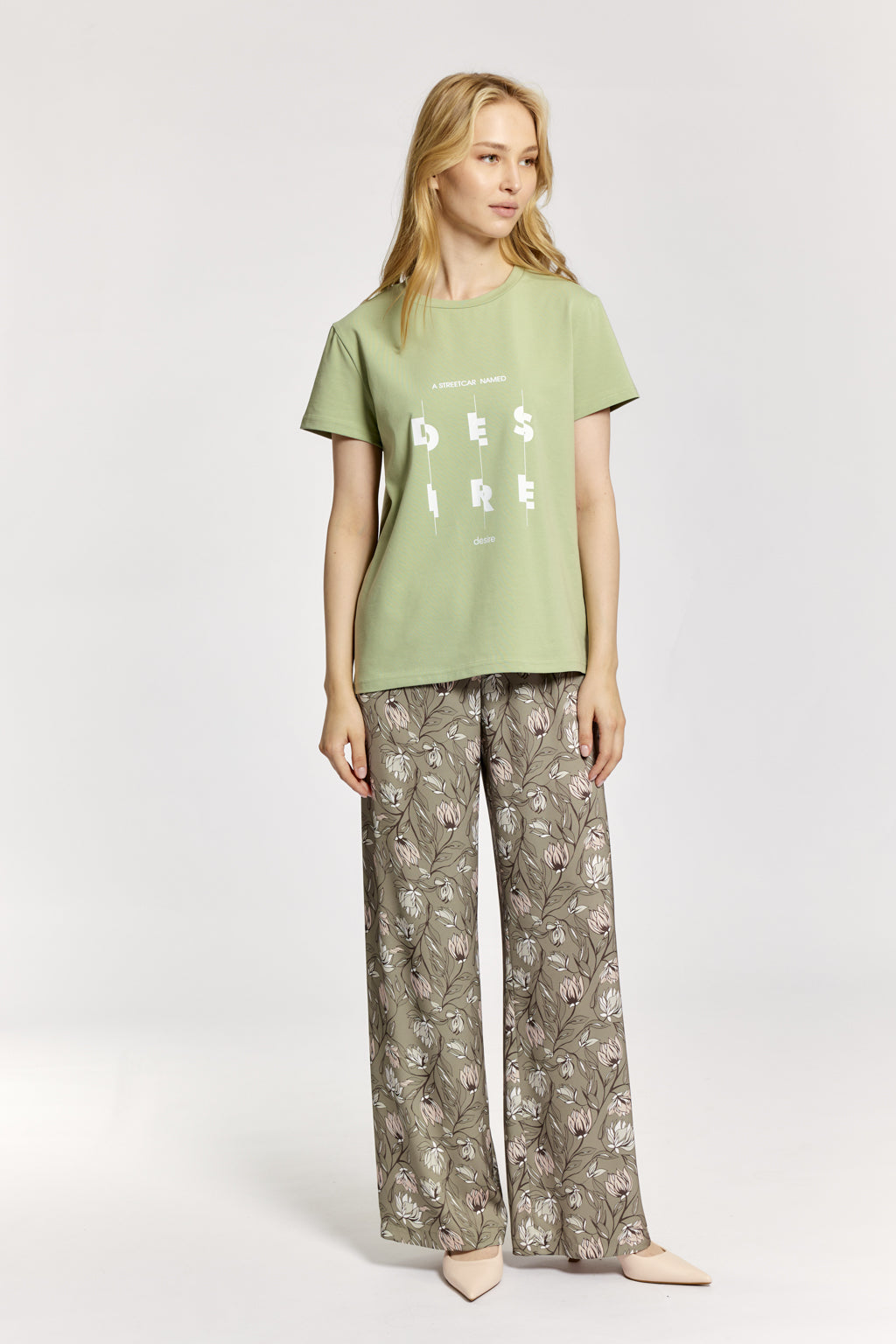 Woman wearing a green t-shirt with text and patterned pants on a white background