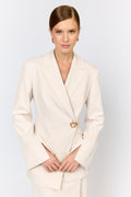 Woman wearing a cream blazer with a gold clasp on a light gray background