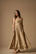Woman wearing AYRA long beige dress featuring multicolored handcrafted floral embroidery on the structured bodice and hemline