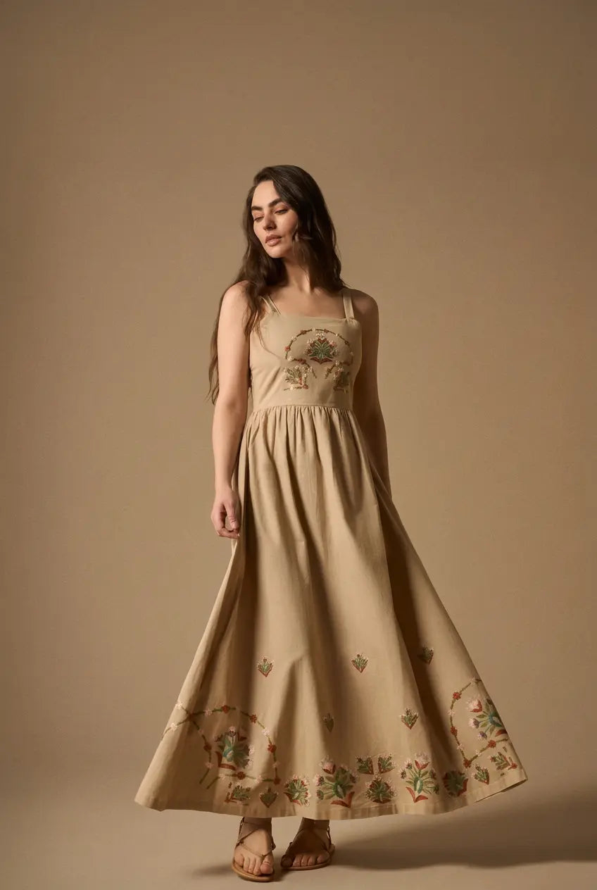 Woman wearing AYRA long beige dress featuring multicolored handcrafted floral embroidery on the structured bodice and hemline
