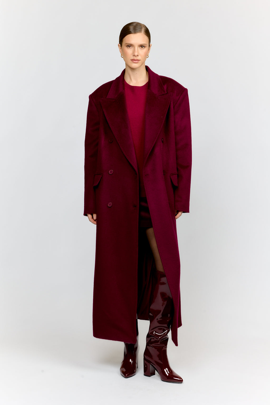 Woman wearing a long burgundy coat and boots on a white background