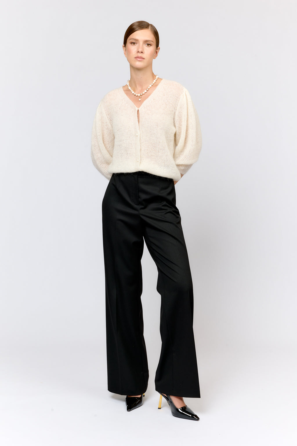 Person wearing a beige cardigan and black pants on a white background