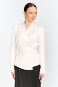 Woman wearing a white wrap-style blouse with black pants on a light gray background