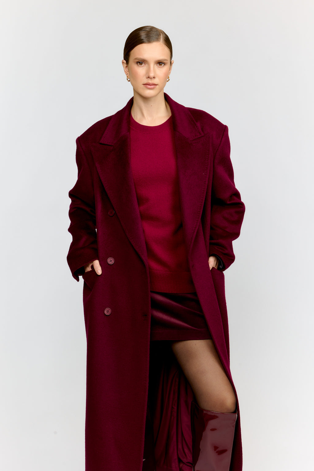 Woman wearing a long burgundy coat over a red dress on a white background
