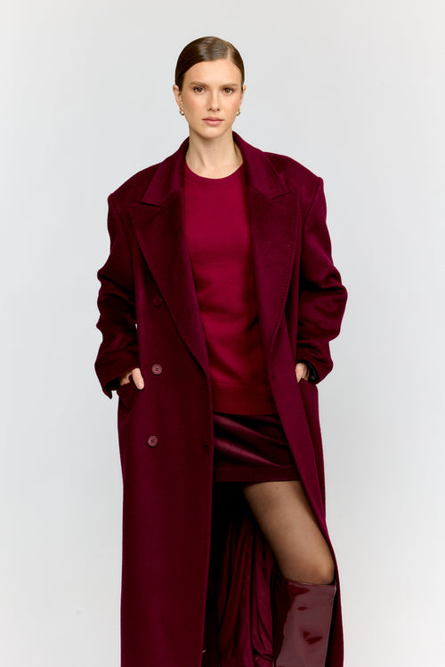 Woman wearing a long burgundy coat over a red dress on a white background