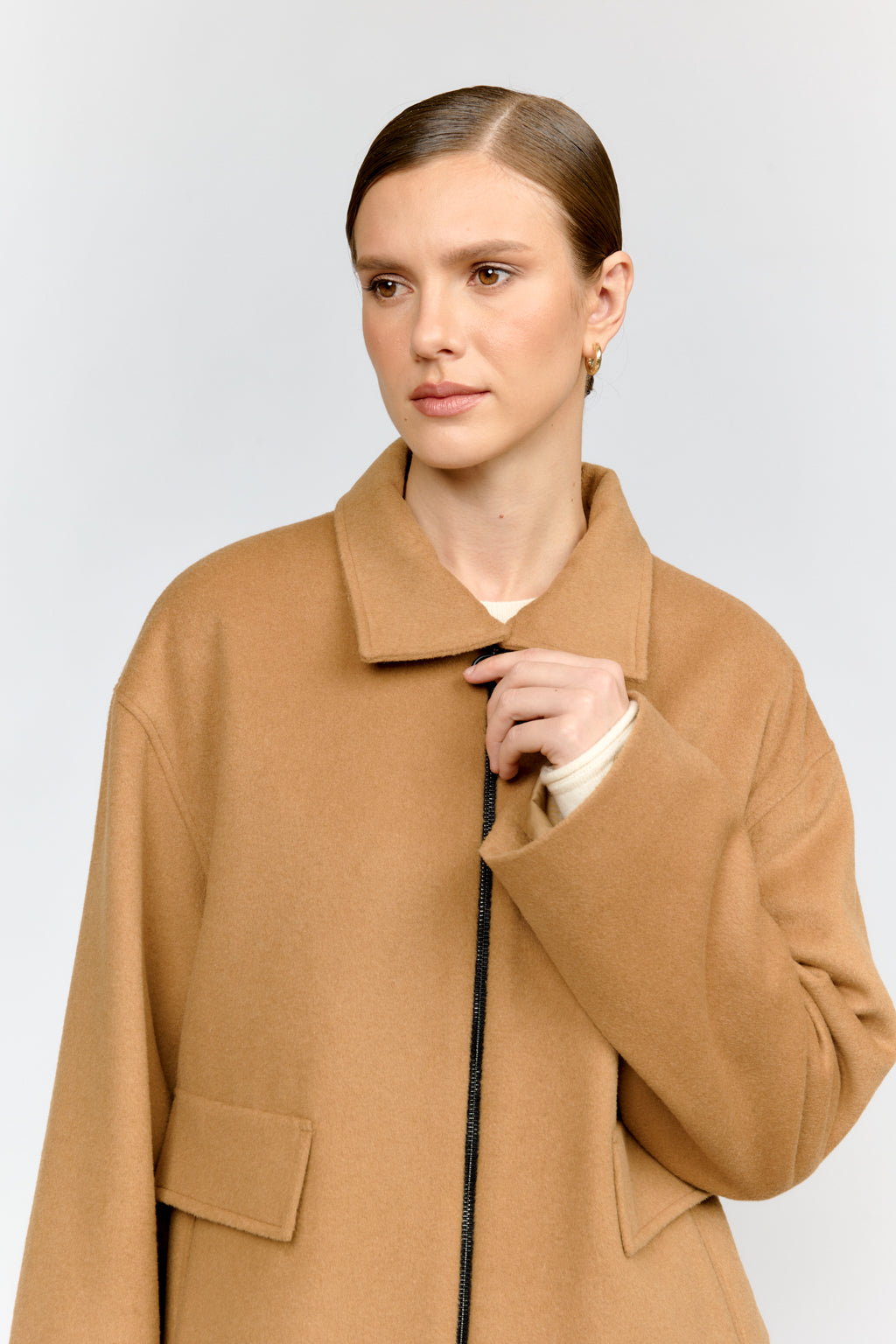 Woman wearing a tan coat against a plain background