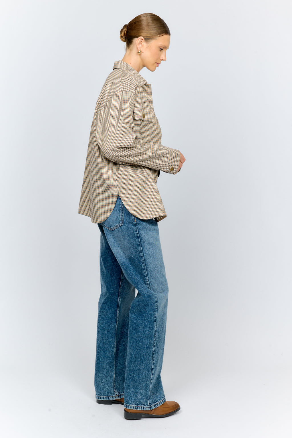Person wearing a beige checkered shirt and blue jeans on a white background