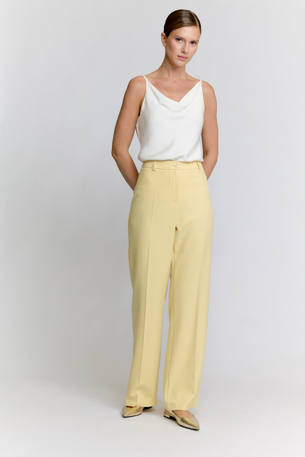 Woman wearing a white top and yellow pants on a light gray background