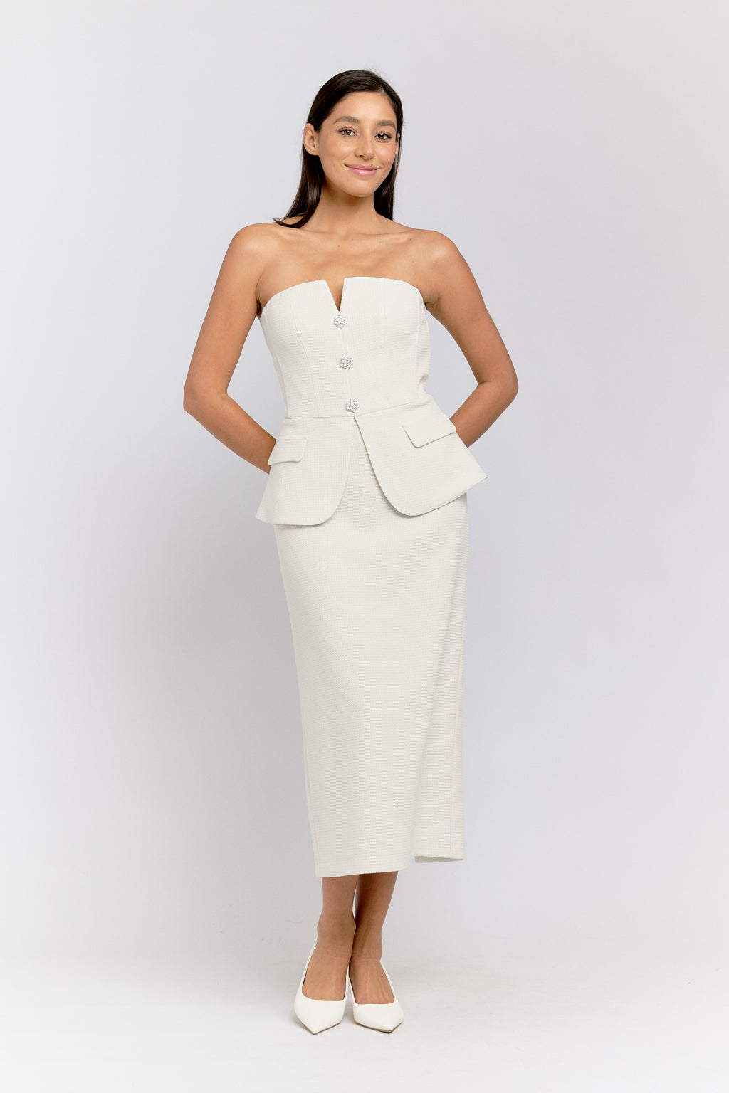 Woman wearing a white strapless dress with a jacket on a plain background