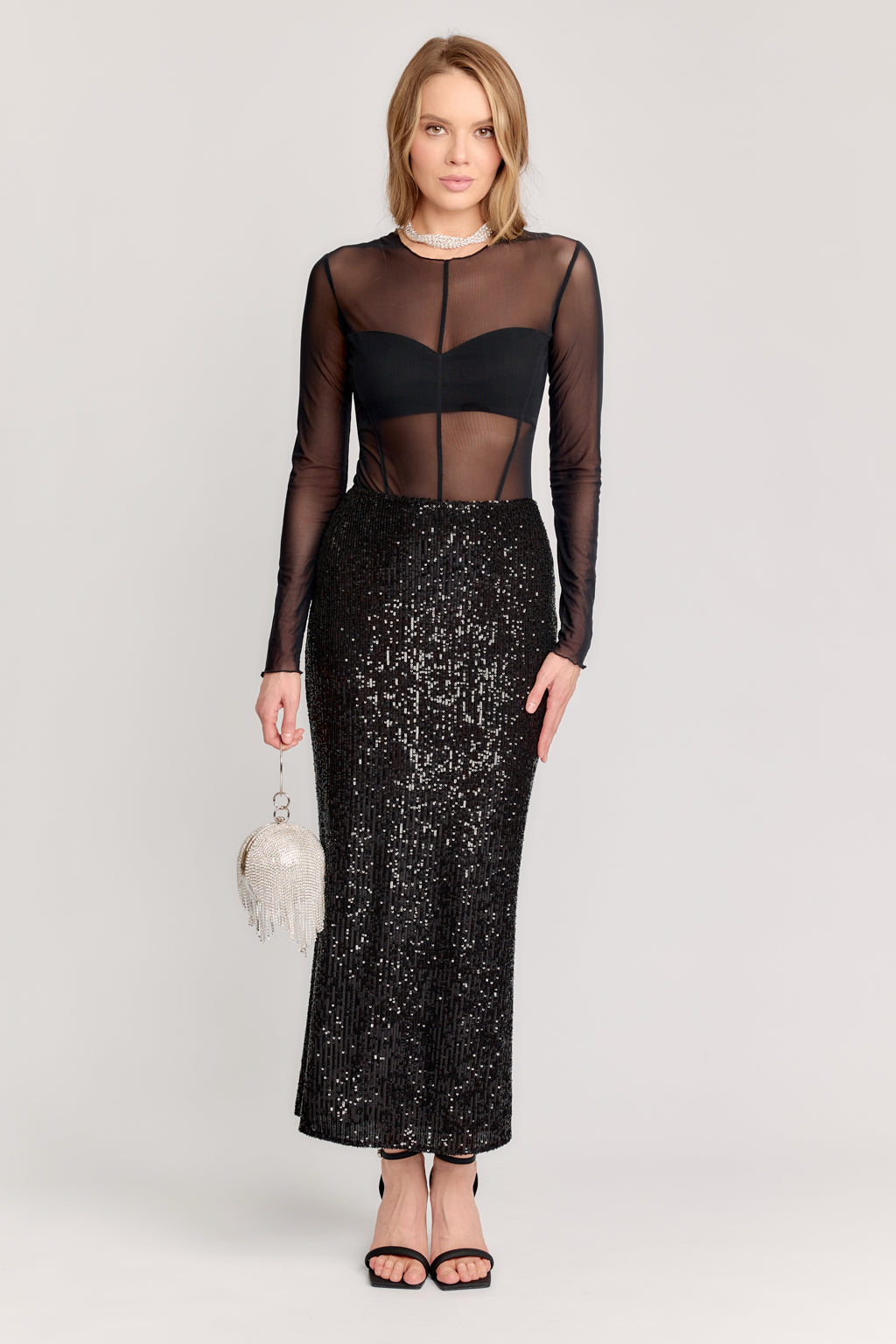 Woman wearing a black sheer top and sequin skirt with a white background