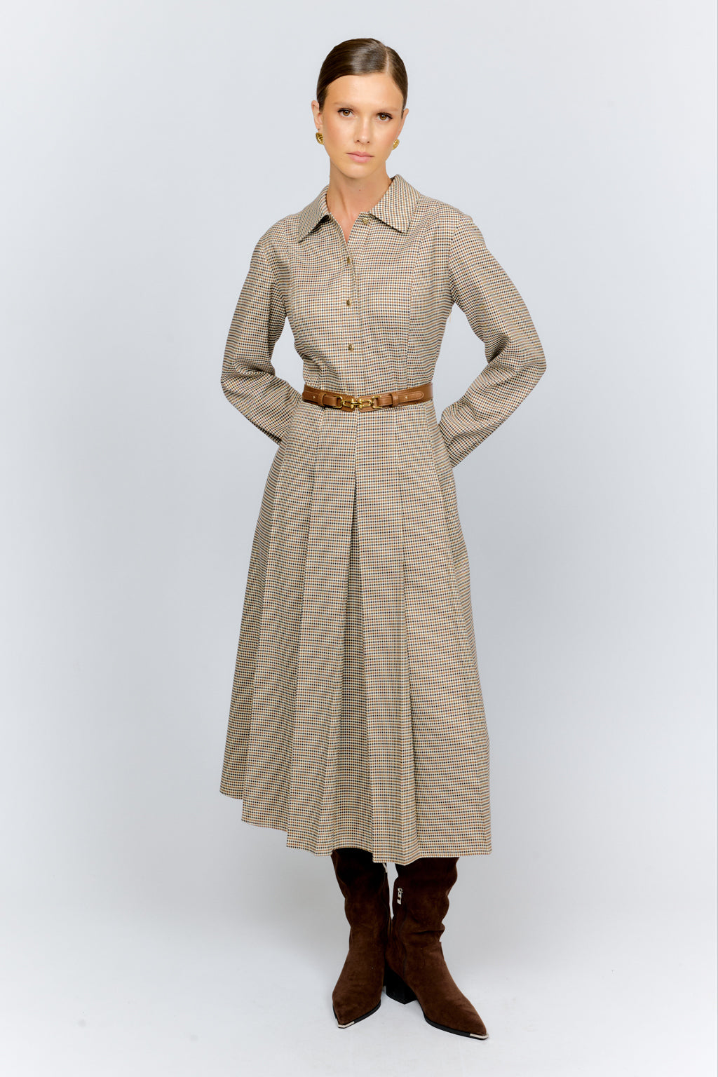 Woman wearing a long beige checkered dress with brown boots on a white background