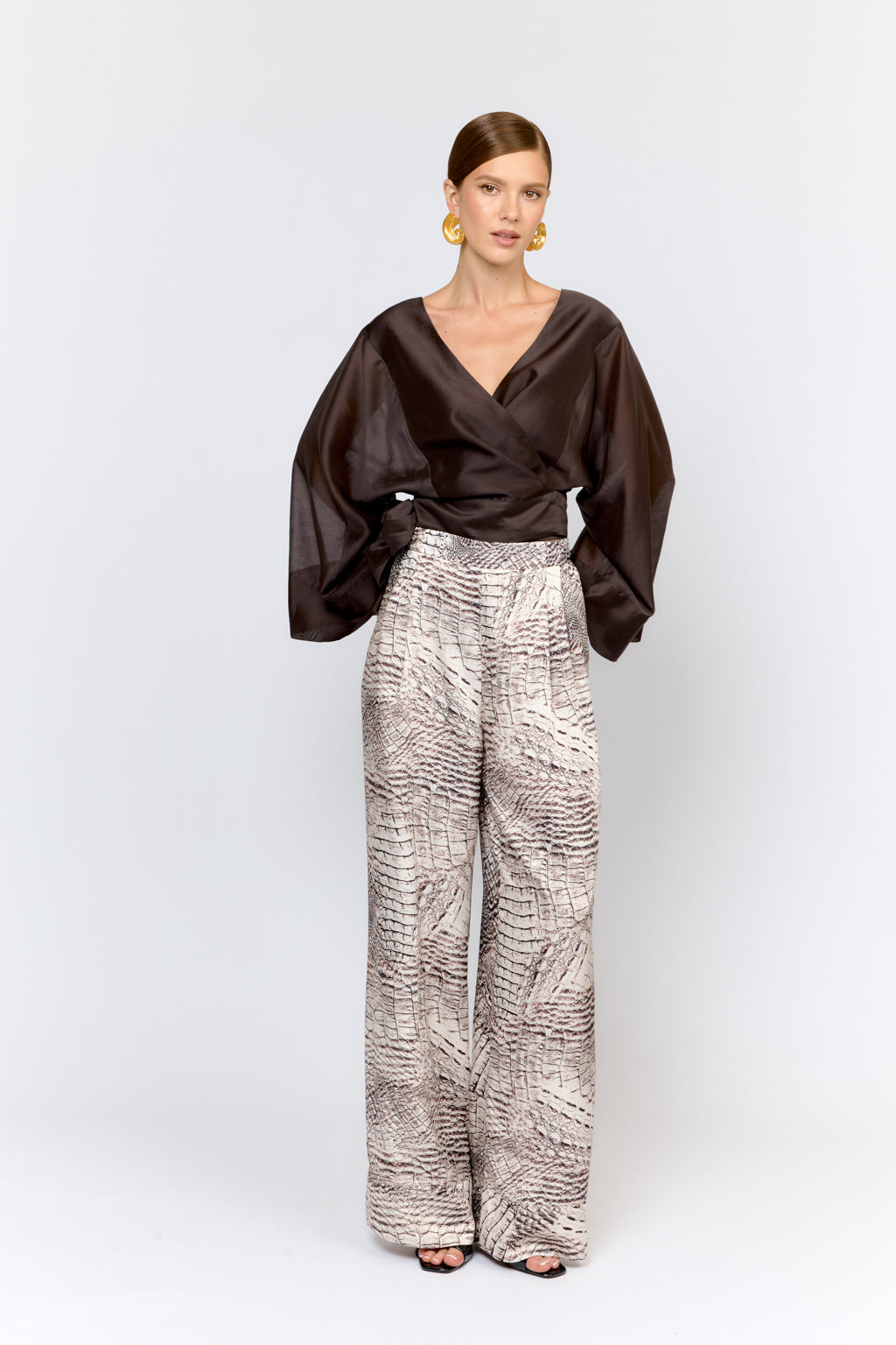 Woman wearing a brown top and patterned pants on a white background