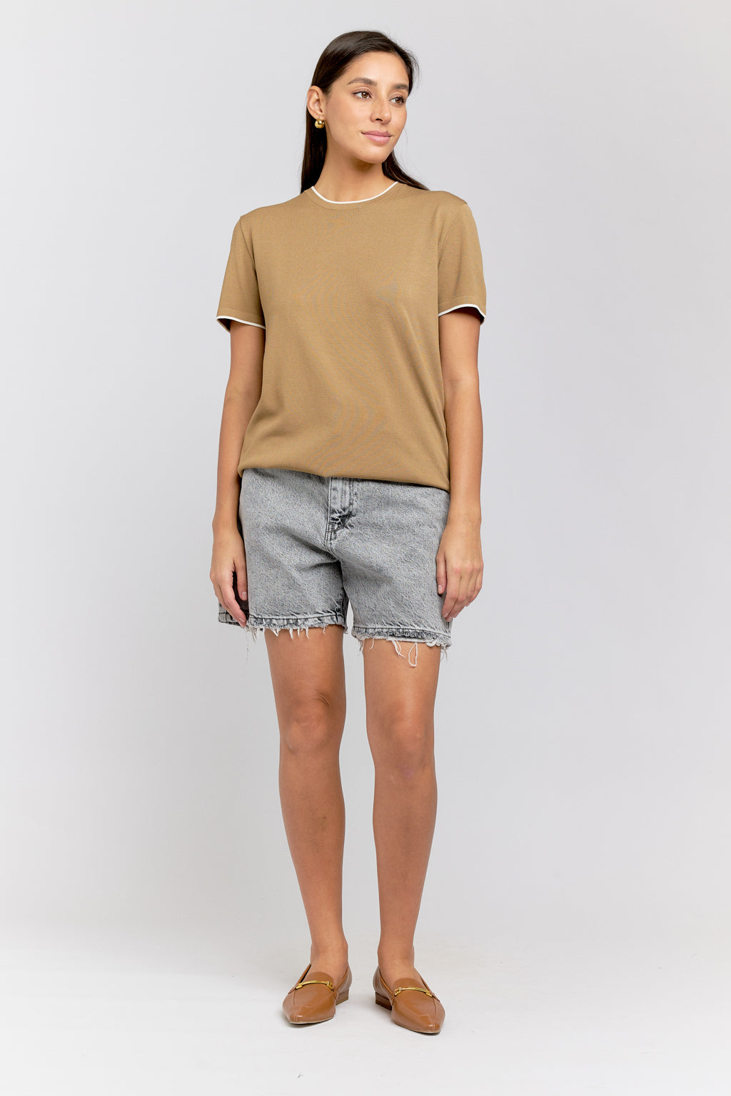 Woman wearing a beige t-shirt and denim shorts on a white background