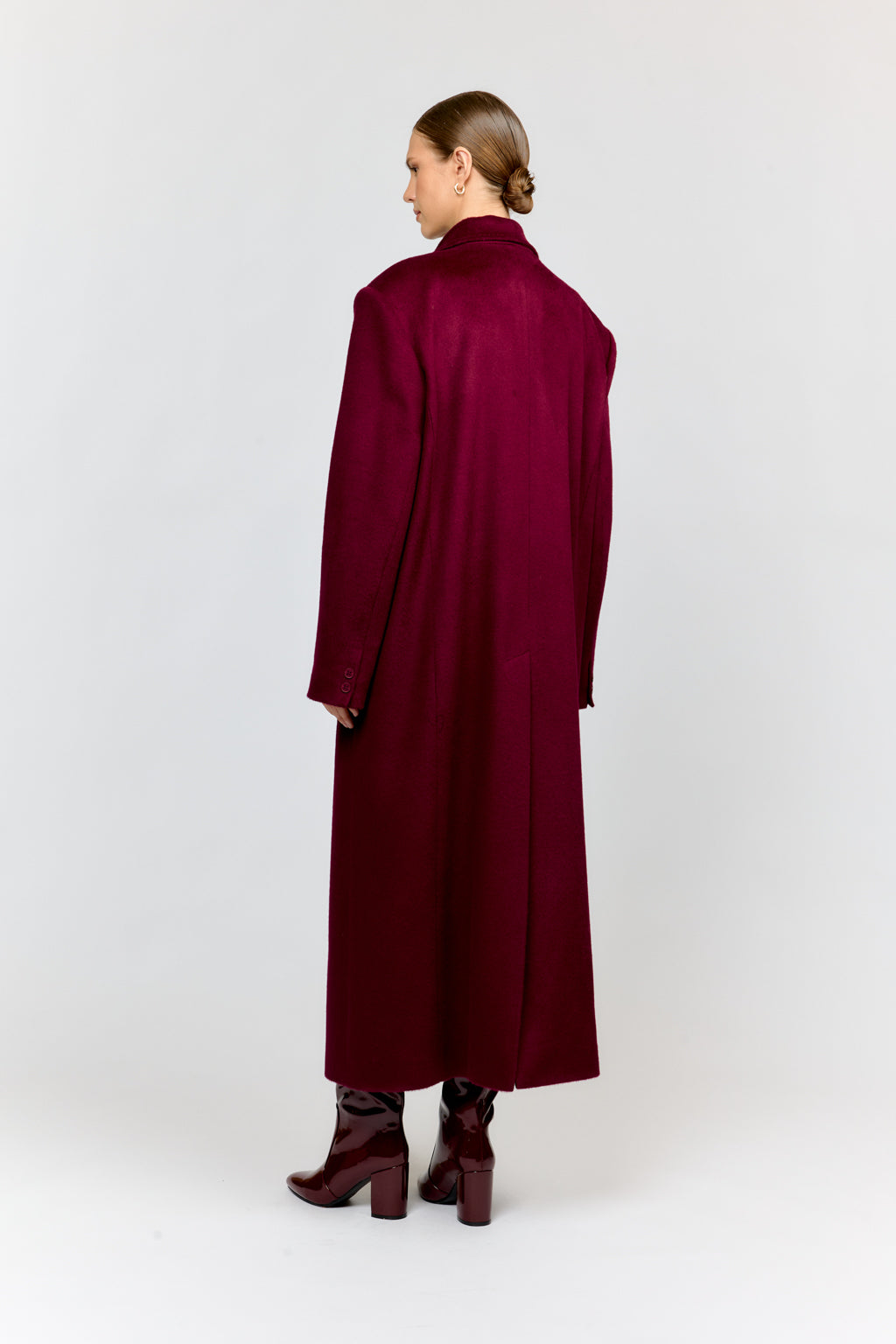 Person wearing a long burgundy coat on a white background