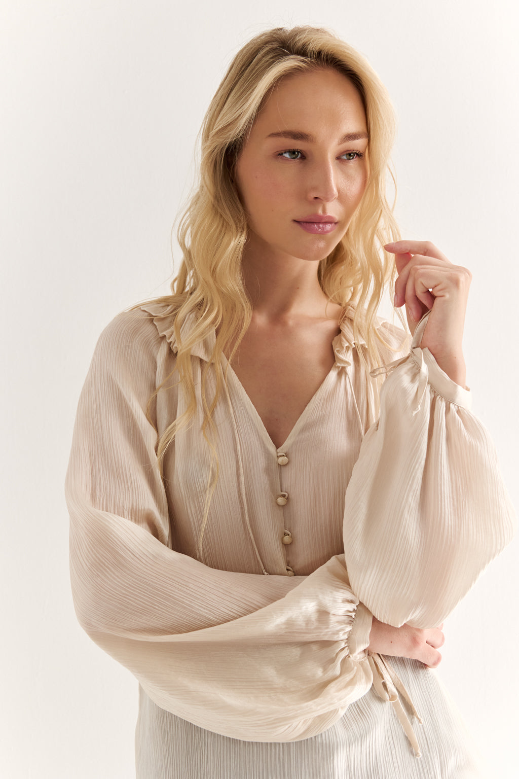 Woman wearing a beige blouse with long sleeves against a white background
