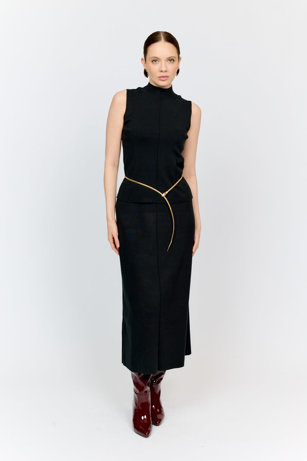 Woman wearing a black sleeveless top and skirt with gold zipper on a white background