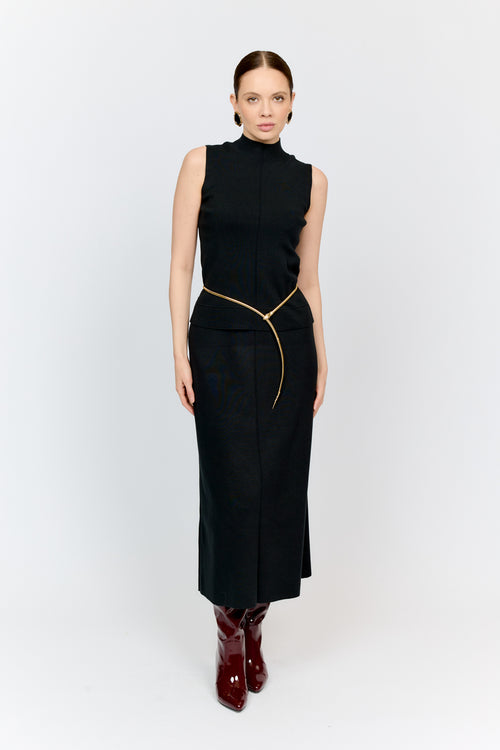 Woman wearing a black sleeveless top and skirt with gold zipper on a white background