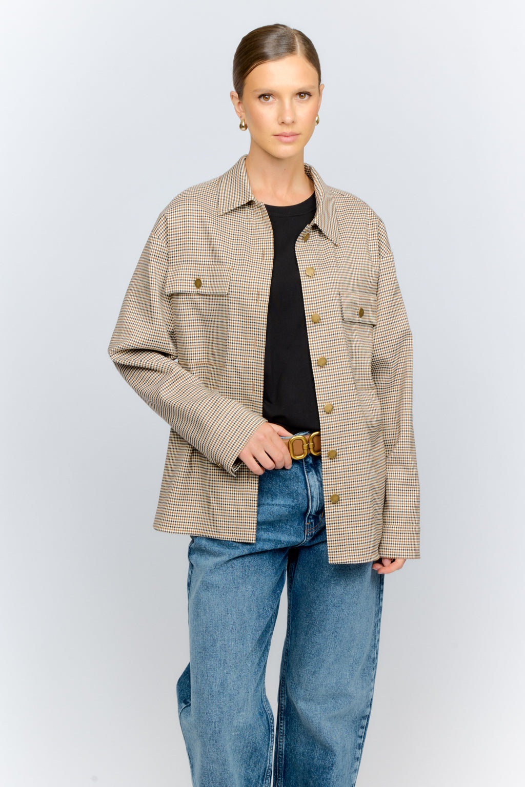 Woman wearing a beige checkered jacket and blue jeans on a light gray background