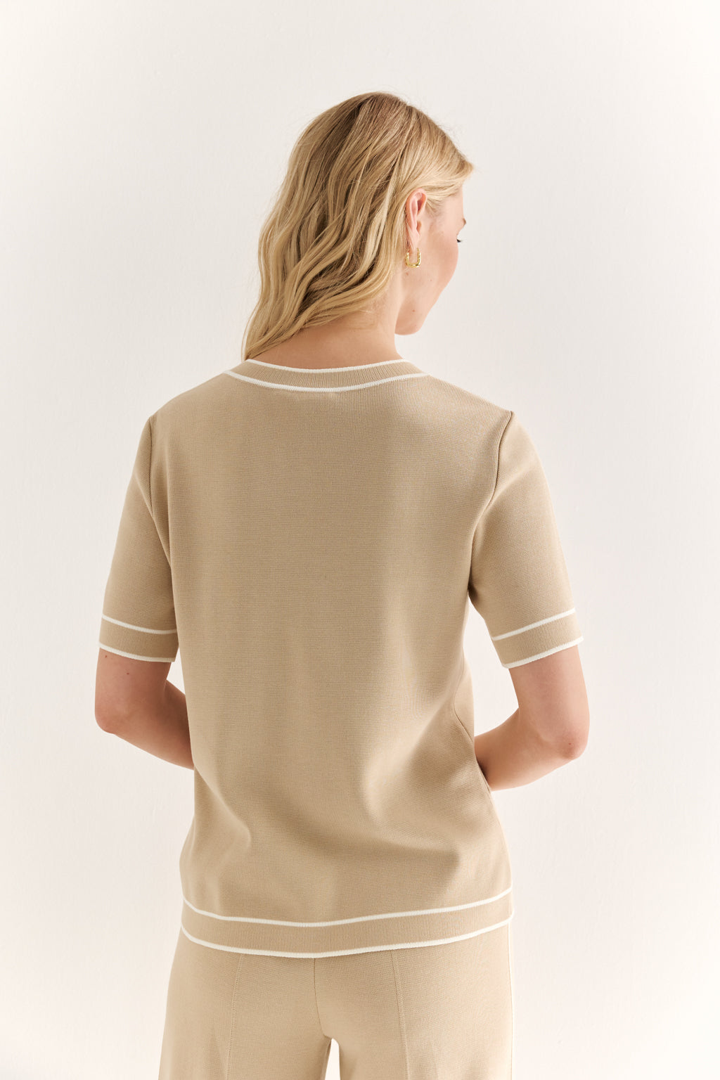 Woman wearing a beige outfit with white trim on a plain background