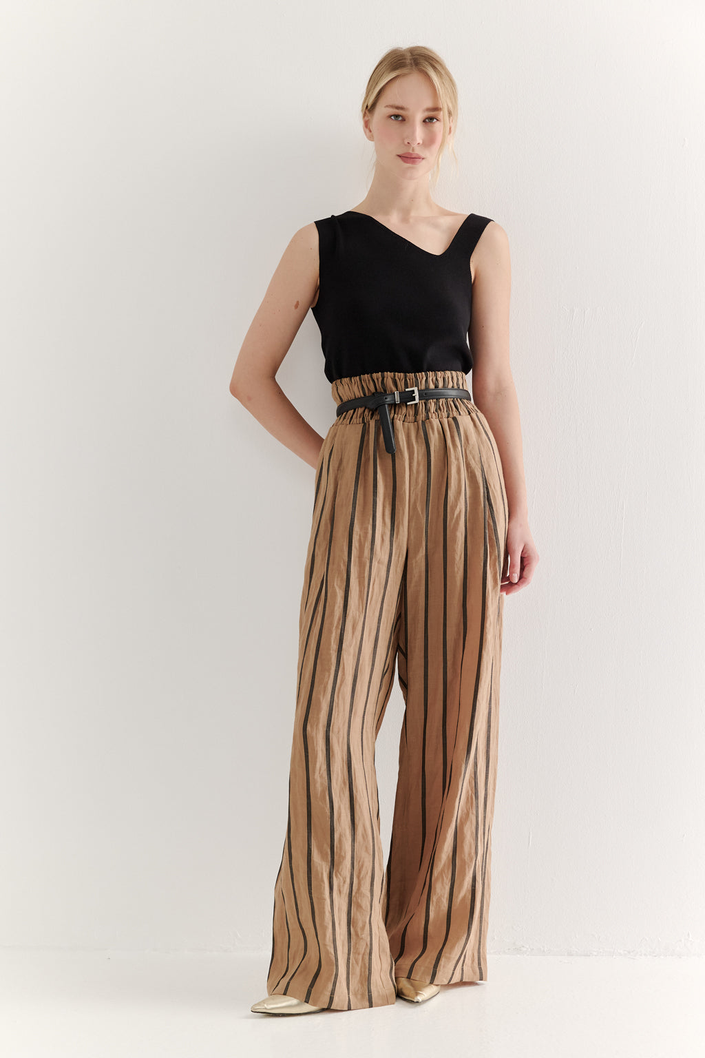 Woman wearing a black sleeveless top and striped pants on a white background