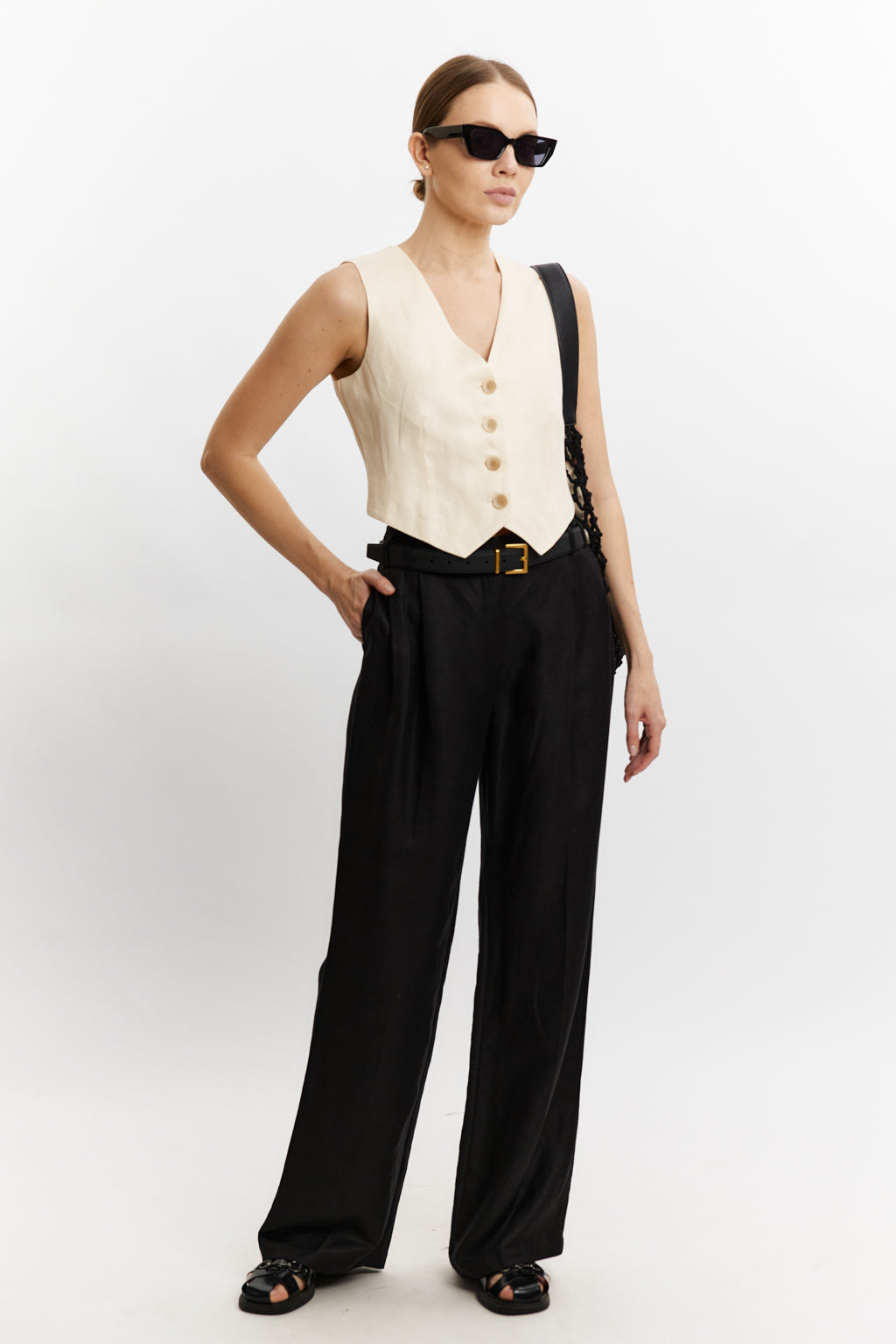 Woman wearing a white vest and black pants with suspenders on a white background