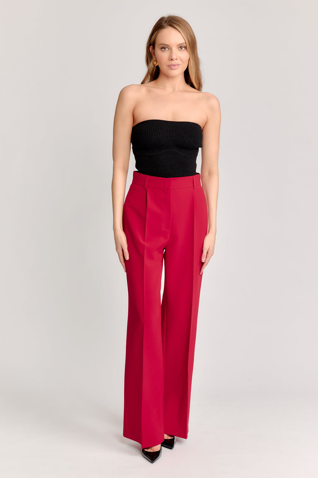 Woman wearing a black strapless top and red high-waisted pants on a light gray background