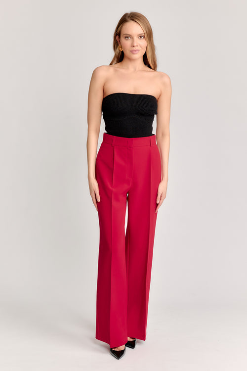 Woman wearing a black strapless top and red high-waisted pants on a light gray background