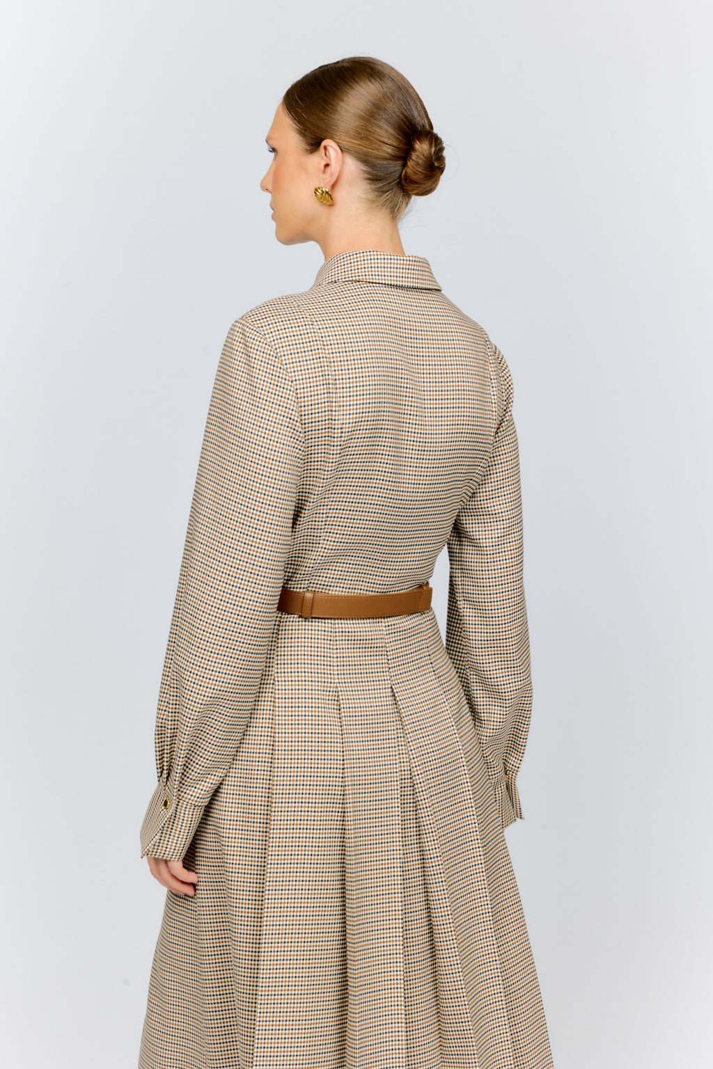 Woman wearing a long, checkered dress with a belt on a white background