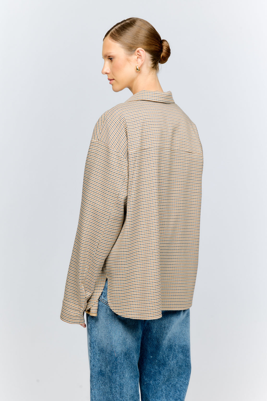 Woman wearing a beige checkered shirt and blue jeans on a white background