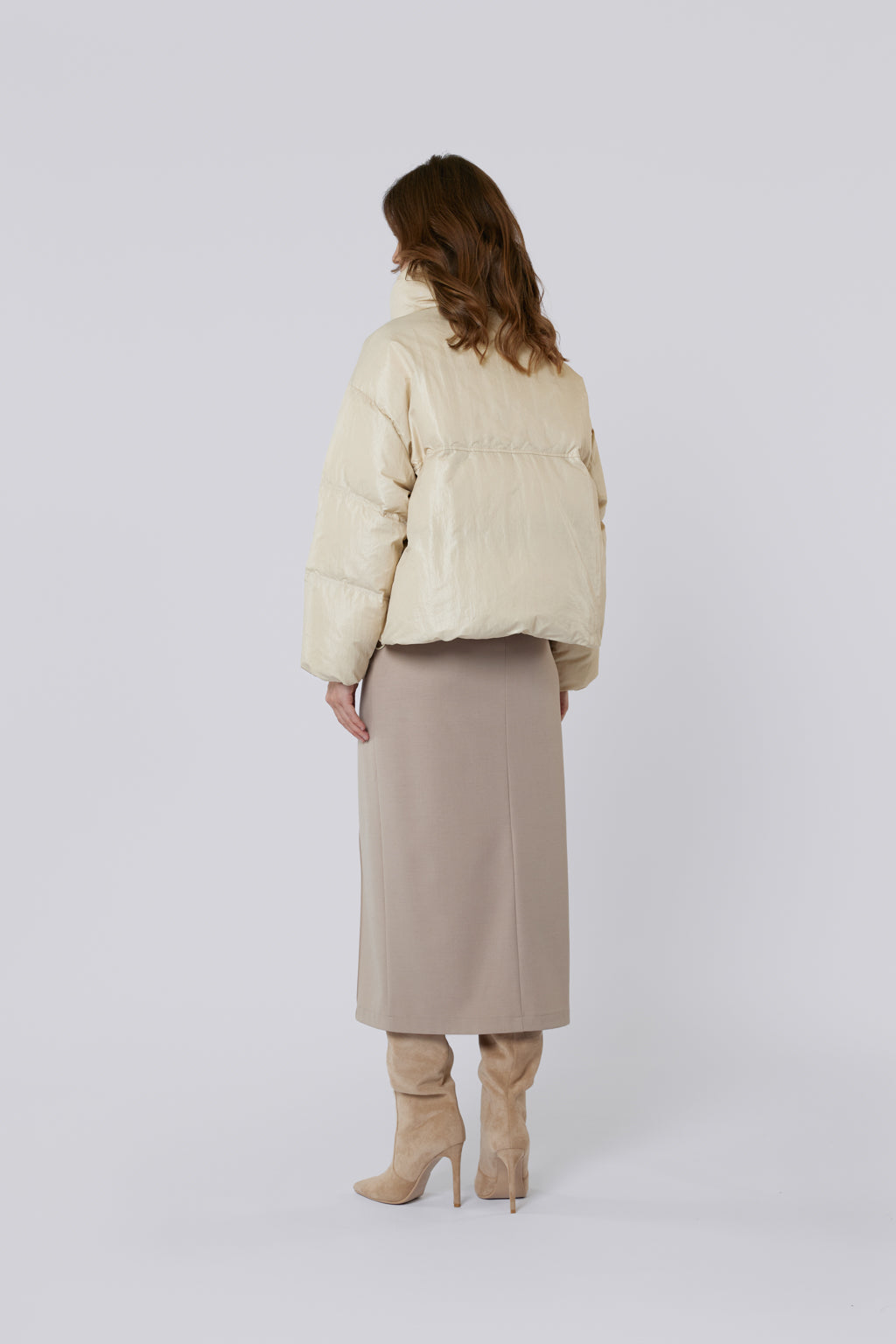 Person wearing a beige puffer jacket and skirt with beige boots on a white background