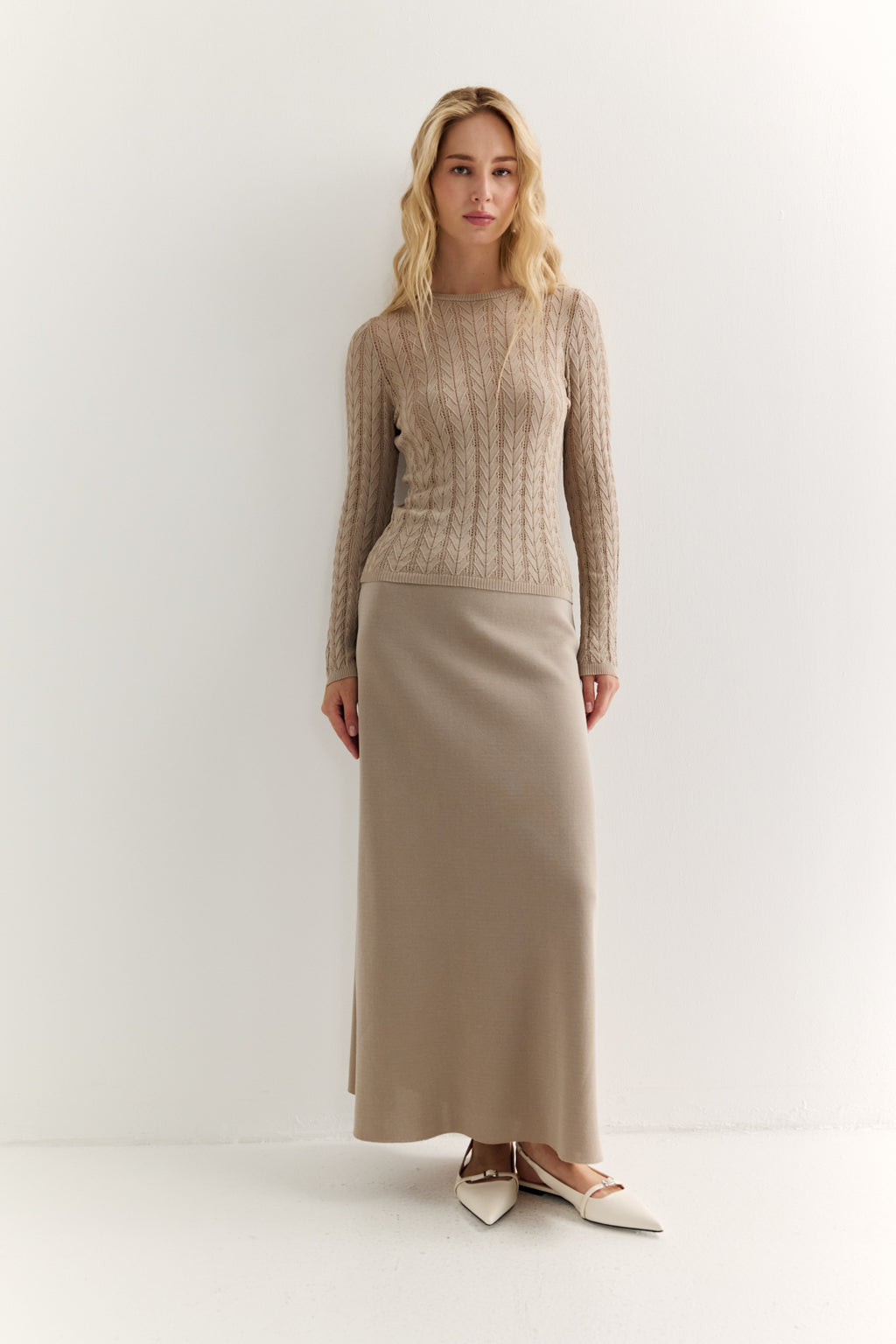 Woman wearing a beige knit sweater and long skirt on a white background