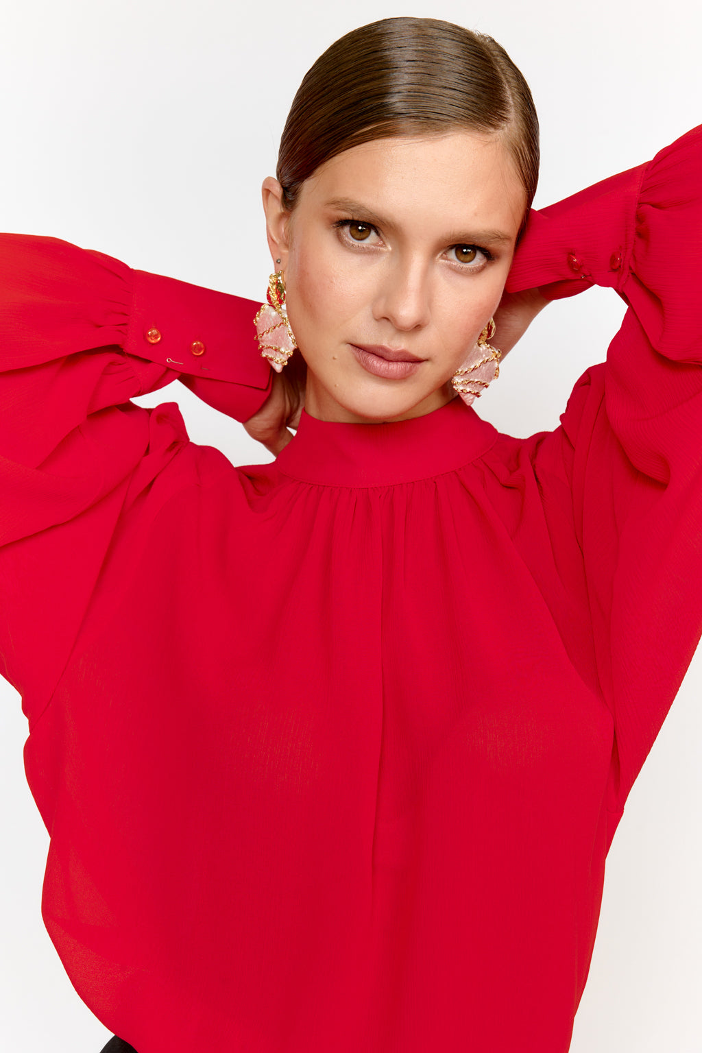 Woman wearing a red blouse with large sleeves against a white background