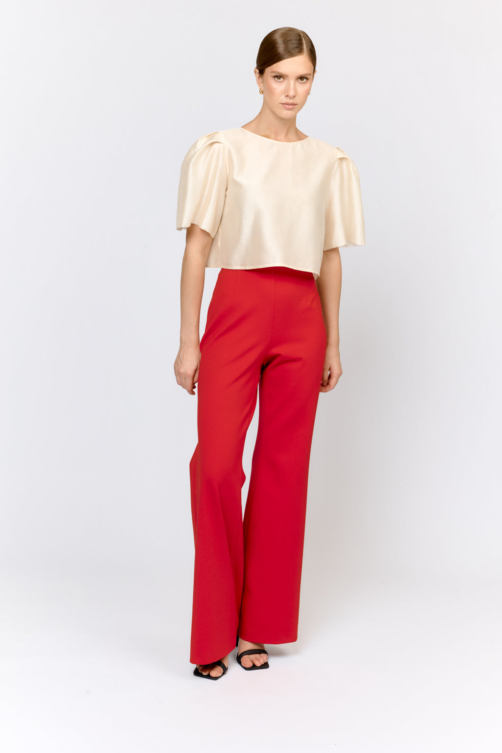 Woman wearing a beige top and red pants on a white background