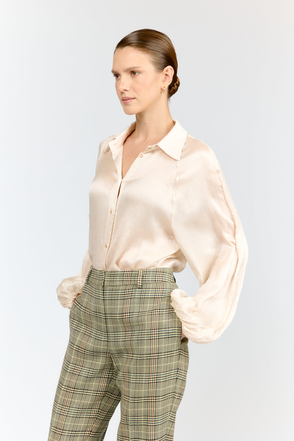 Woman wearing a light pink satin shirt and plaid pants on a white background