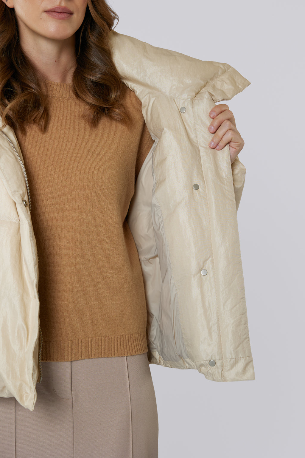 Person wearing a beige puffer jacket over a brown sweater on a white background