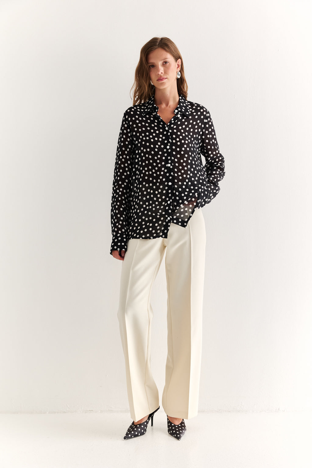 Woman wearing a black polka dot blouse and white pants on a white background