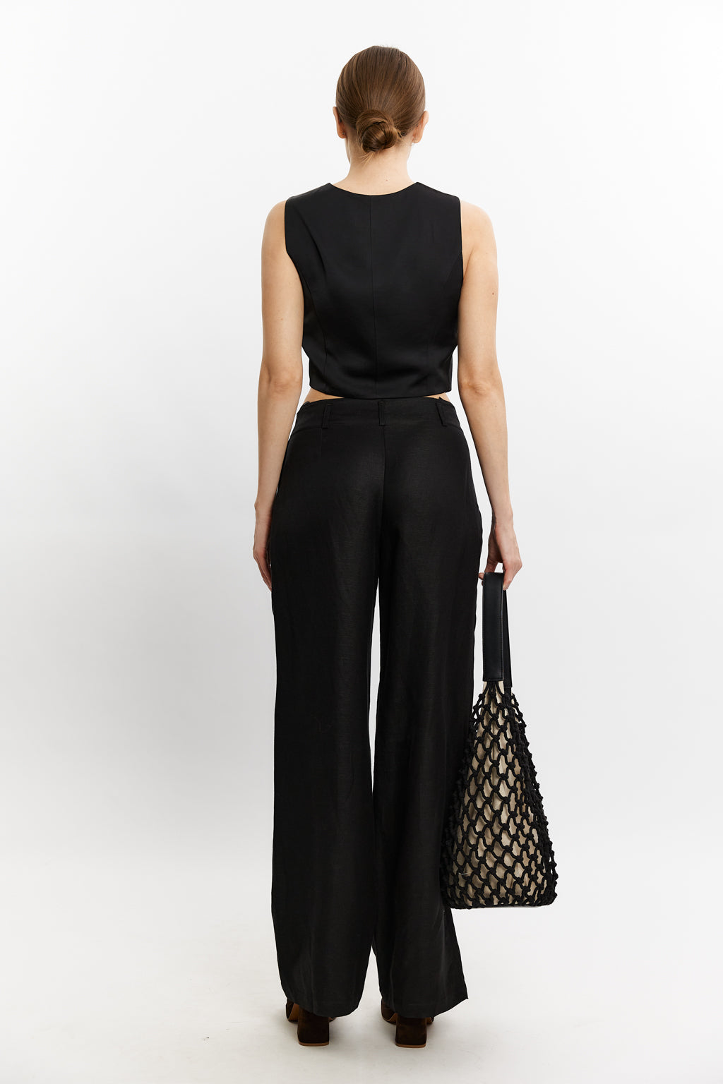 Woman wearing a black sleeveless top and wide-leg pants, holding a black mesh bag on a white background