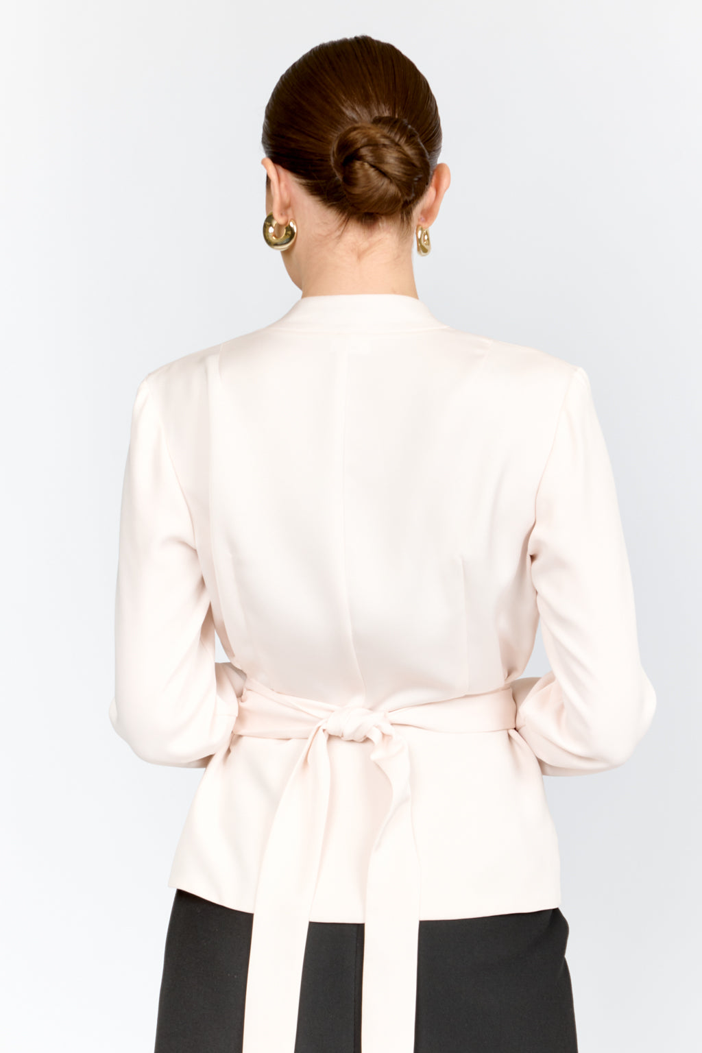 Person wearing a white blouse with a tie waist on a plain background
