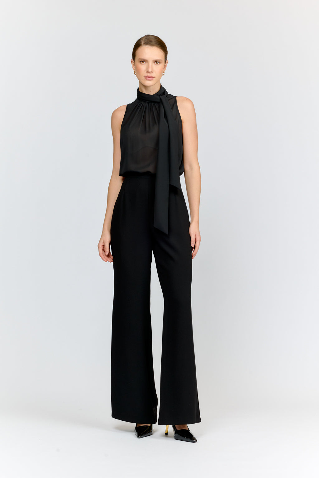 Woman wearing a black sleeveless top and wide-leg pants on a white background