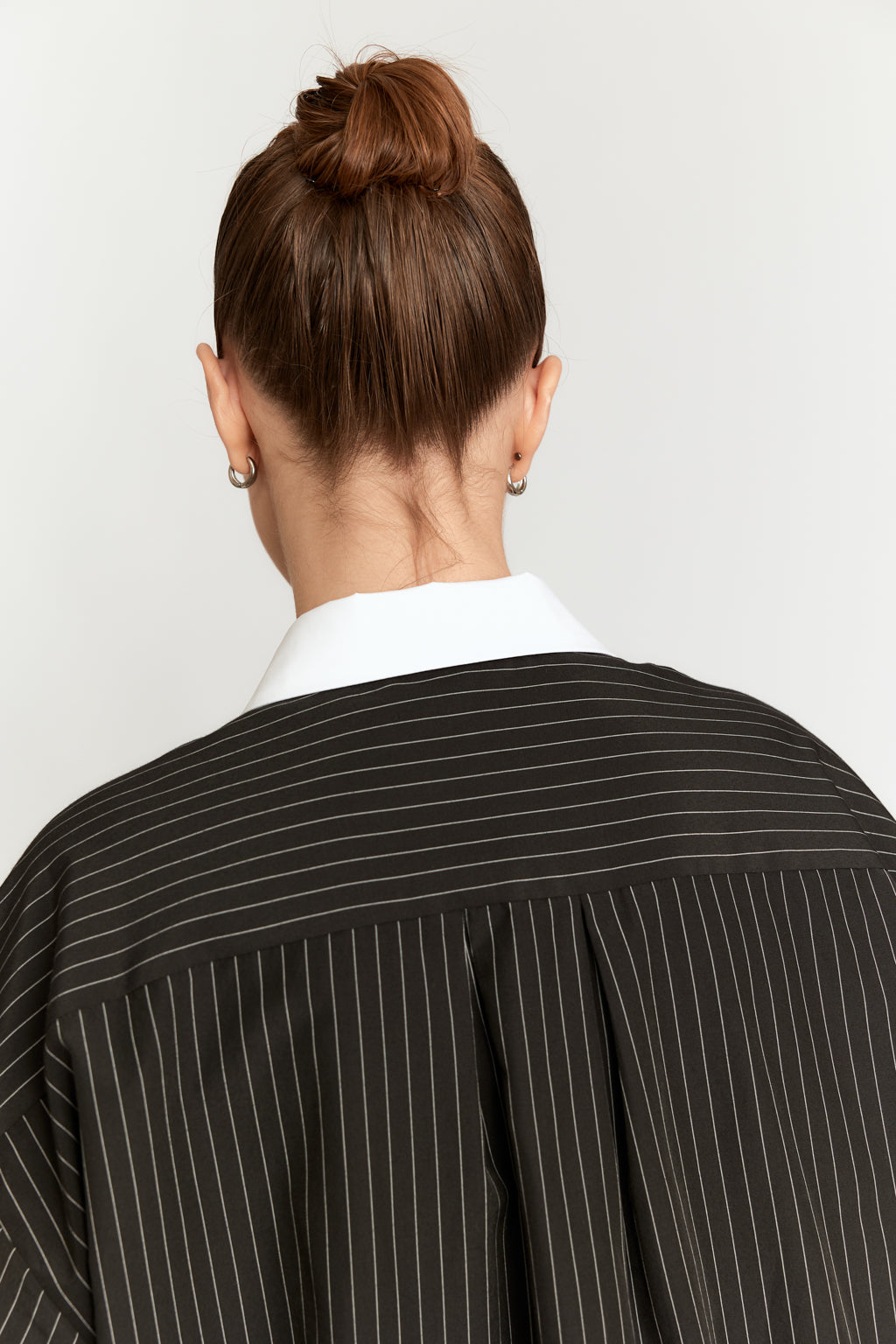 Person wearing a black pinstripe shirt with a white collar against a plain background