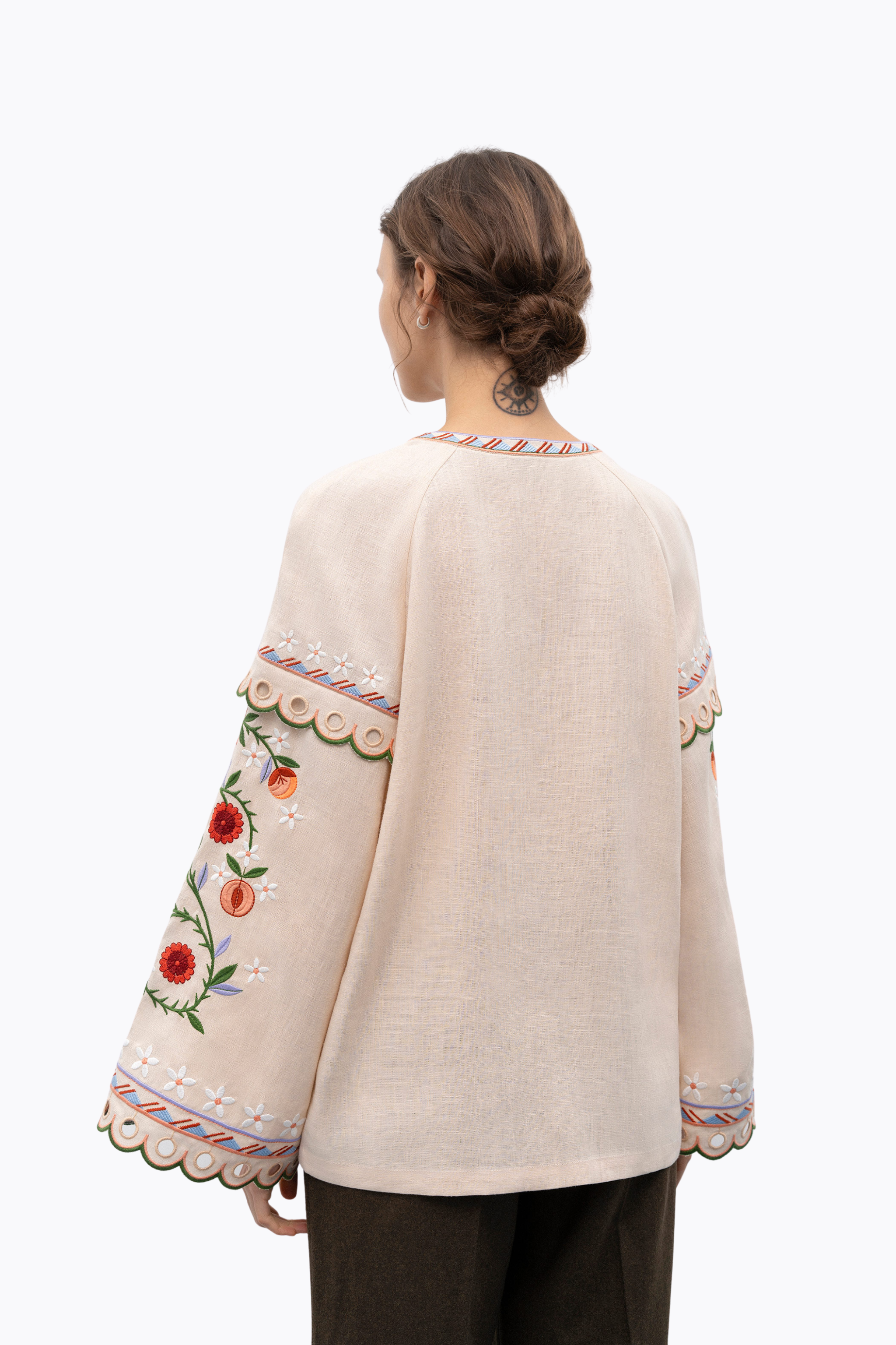 Woman wearing a cream-colored embroidered blouse with floral patterns on a white background