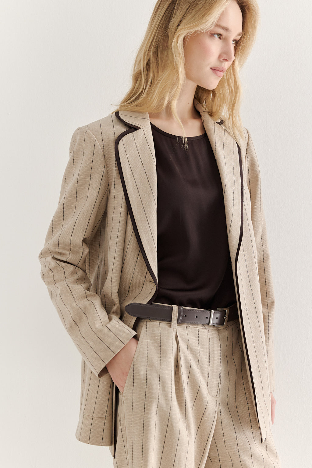 Woman wearing a beige pinstripe suit with a black top on a white background