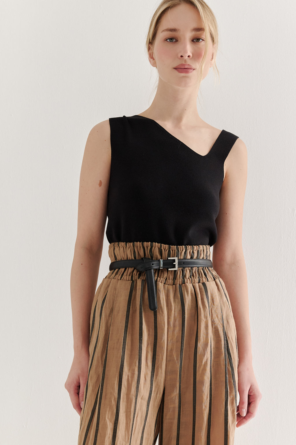Woman wearing a black sleeveless top and striped pants on a plain background