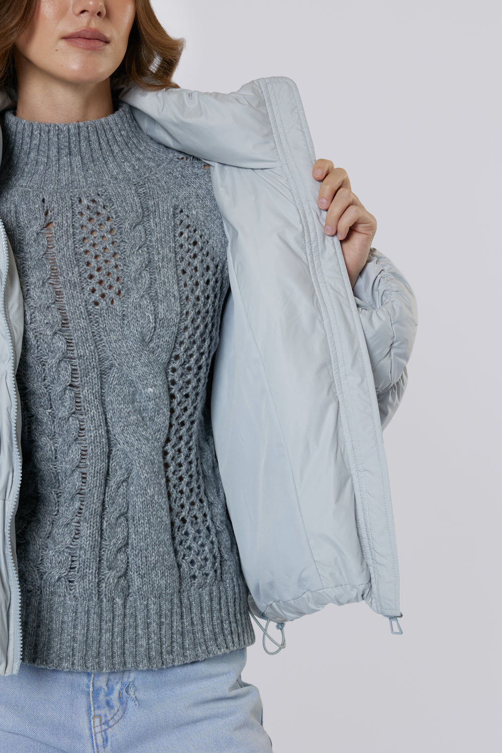 Person wearing a gray cable knit sweater with a light blue jacket over it on a white background