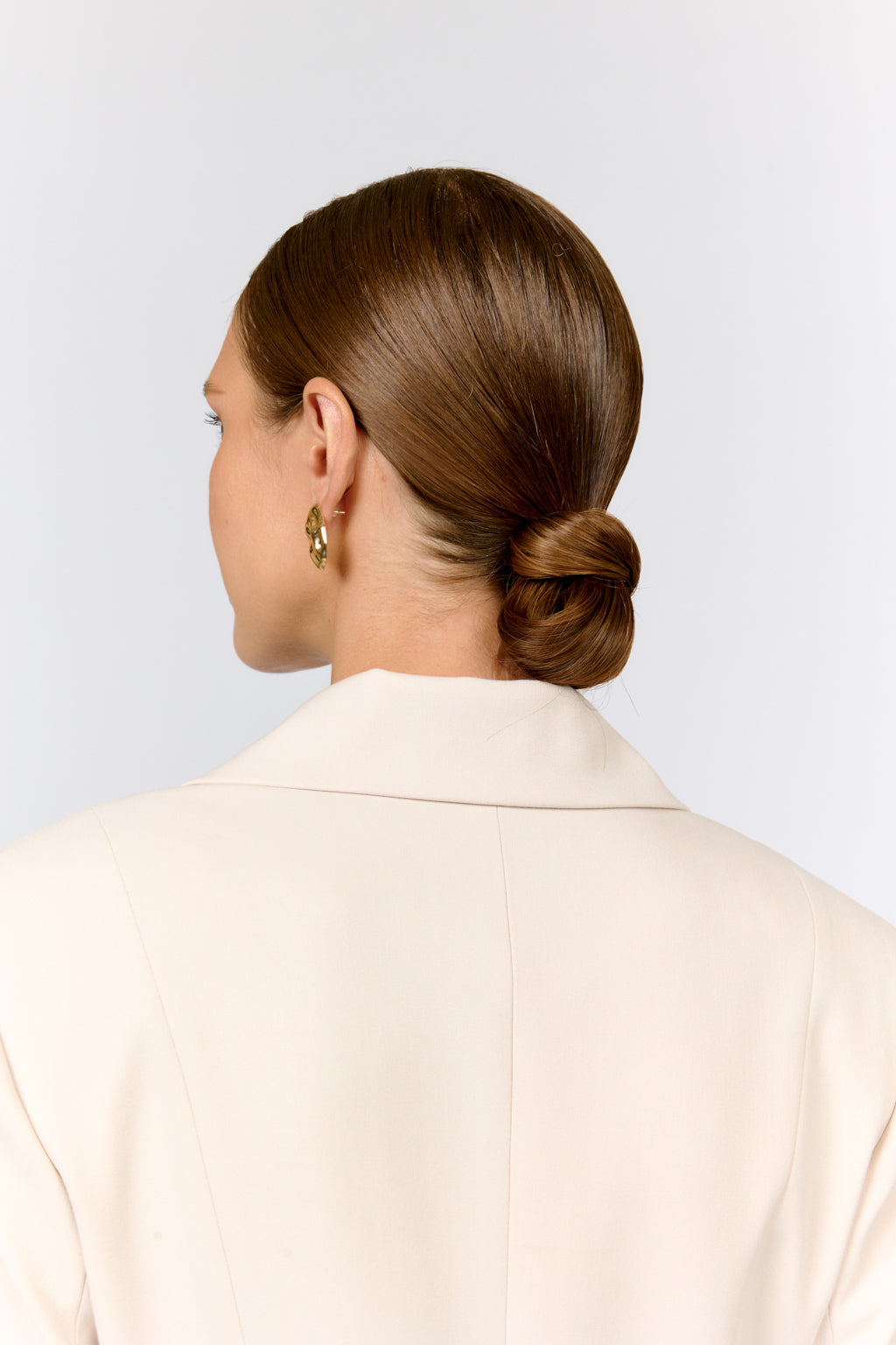 Woman with a styled bun wearing a beige jacket on a light gray background