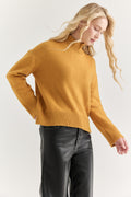 Woman wearing a mustard yellow sweater and black pants on a white background