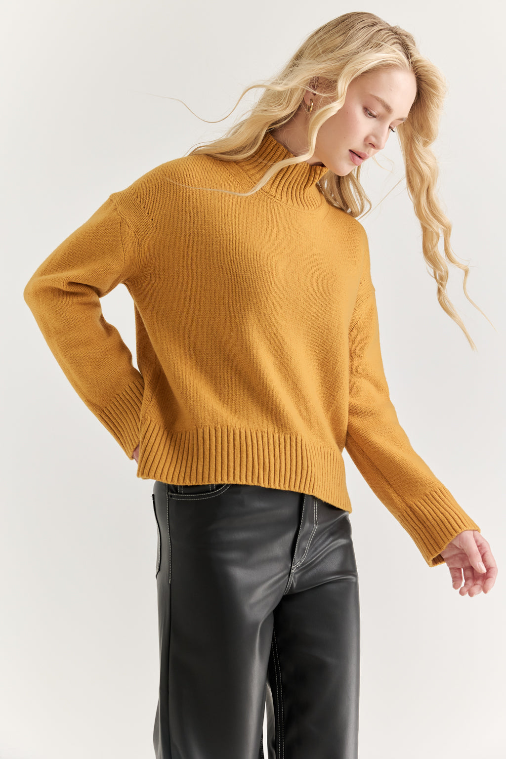 Woman wearing a mustard yellow sweater and black pants on a white background