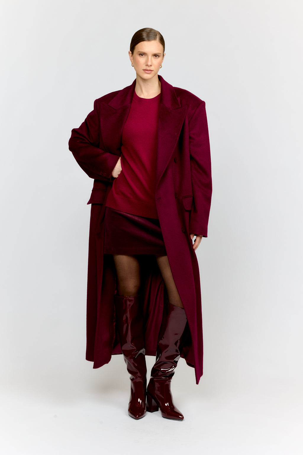 Woman wearing a burgundy coat, dress, and boots on a white background