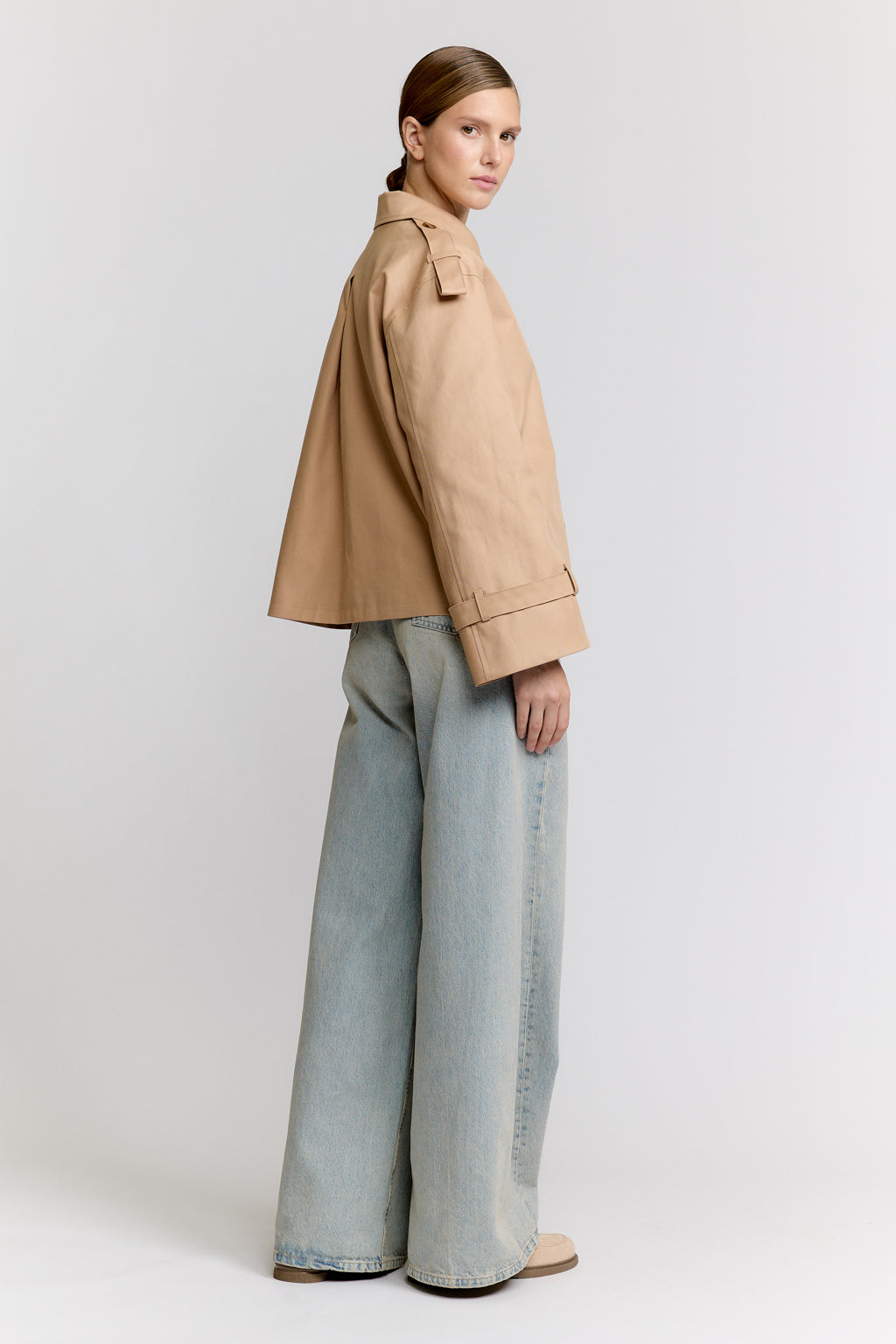 Woman wearing a beige jacket and light blue jeans on a white background