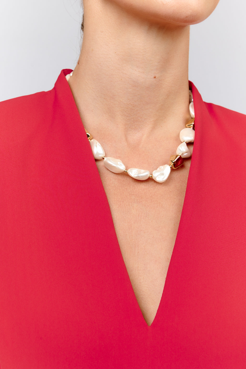 Pearl bracelet on a person wearing a red top against a light gray background